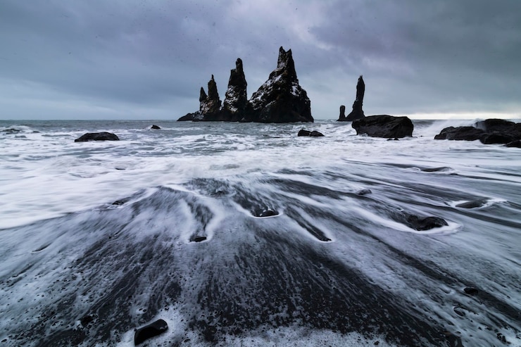 Foto basalt-felsformationen troll zehen am schwarzen strand bei sturm reynisdrangar vik island