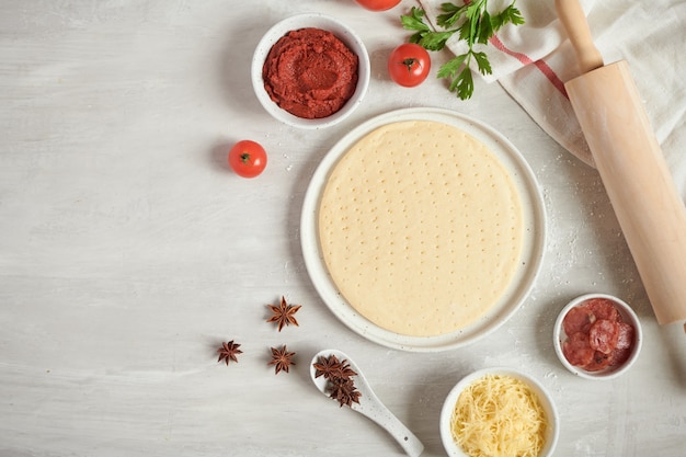 Base de pizza de masa fresca e ingredientes sobre una mesa blanca