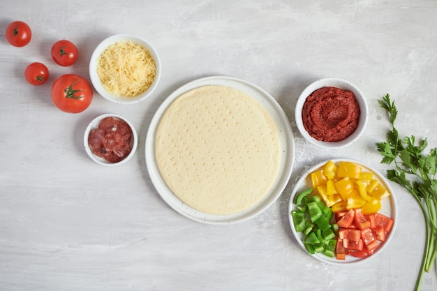 Base de pizza de masa fresca e ingredientes sobre una mesa blanca