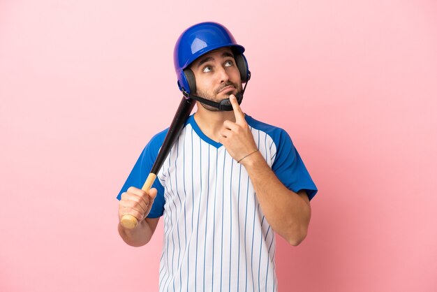 Baseballspieler mit Helm und Schläger einzeln auf rosa Hintergrund, der beim Nachschlagen Zweifel hat