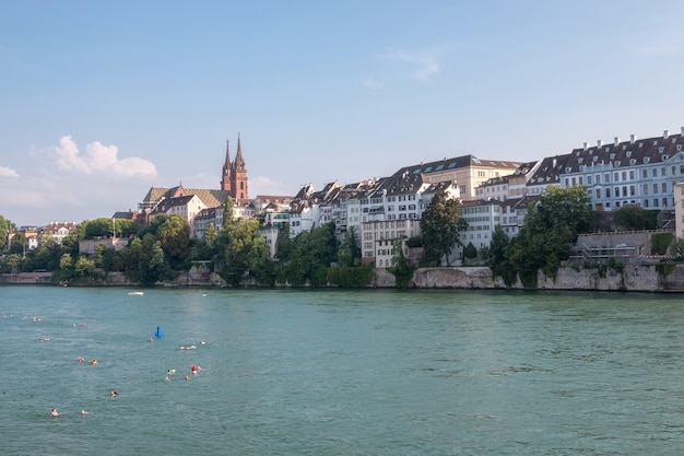 Basel, Schweiz - 23. Juni 2017: Blick auf die Stadt Basel und den Rhein. Sommerlandschaft, Sonnenscheinwetter, blauer Himmel und sonniger Tag. Menschen schwimmen im Fluss