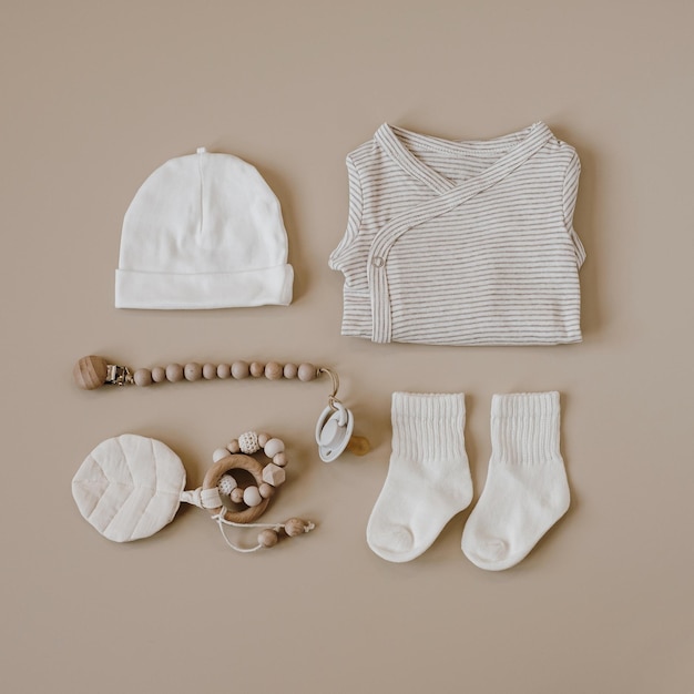 Foto basic-body, mütze, socken, schnuller mit halter, kleidung und accessoires für neugeborene auf neutralem pastellbeigem hintergrund, modische skandinavische kleidung für neugeborene, flache lage von oben