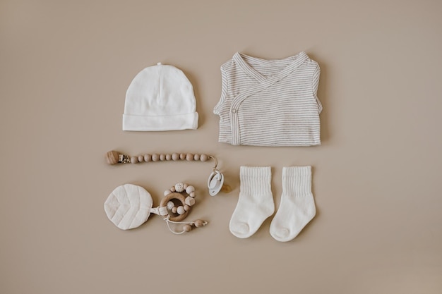 Basic-Body, Mütze, Socken, Schnuller mit Halter, Kleidung und Accessoires für Neugeborene auf neutralem pastellbeigem Hintergrund, modische skandinavische Kleidung für Neugeborene, flache Lage von oben