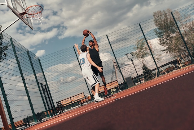 Basketball spielen. Zwei junge Männer in Sportkleidung spielen Basketball, während sie Zeit im Freien verbringen