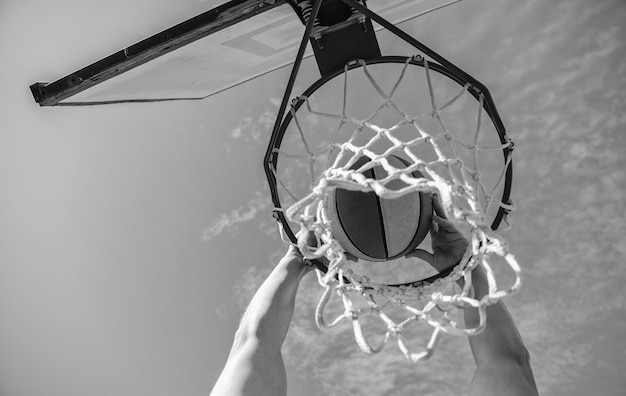 Basketballball fliegt durch Korb in den Händen des Spielers auf Himmelshintergrund Basketball