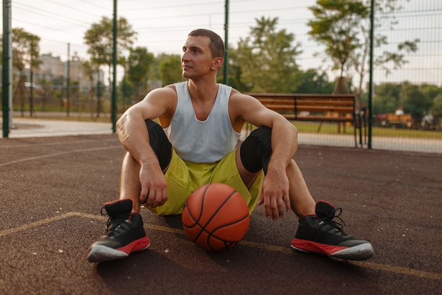 Basketballspieler, der auf dem Boden auf dem Außenplatz sitzt.
