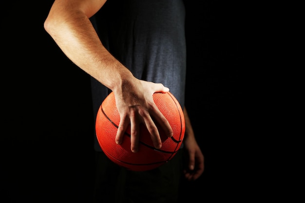 Basketballspieler, der Ball auf dunklem Hintergrund hält