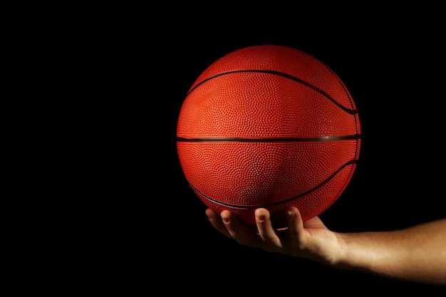 Basketballspieler, der Ball auf dunklem Hintergrund hält