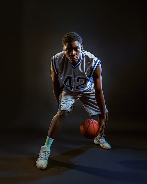 Basketballspieler mit Ball, der in Aktion übt. Professioneller männlicher Baller in Sportbekleidung, der Sportspiel spielt, großer Sportler