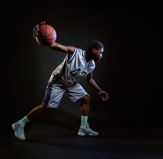 Basketballspieler mit Ball, der in Aktion übt. Professioneller männlicher Baller in Sportbekleidung, der Sportspiel spielt, Sportler