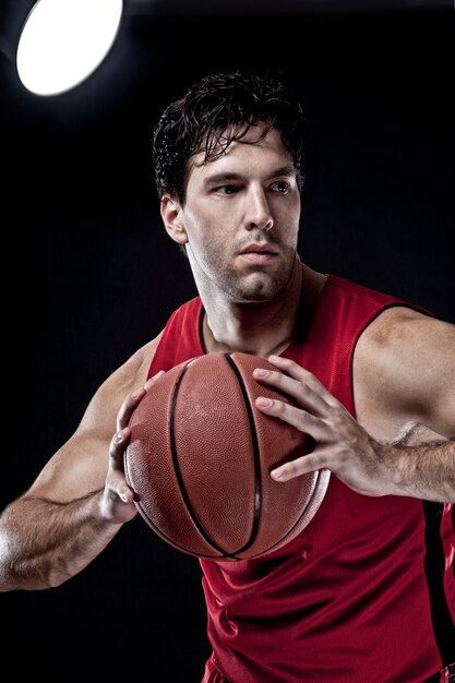 Basketballspieler mit einem Ball in den Händen und einer roten Uniform. Fotostudio.