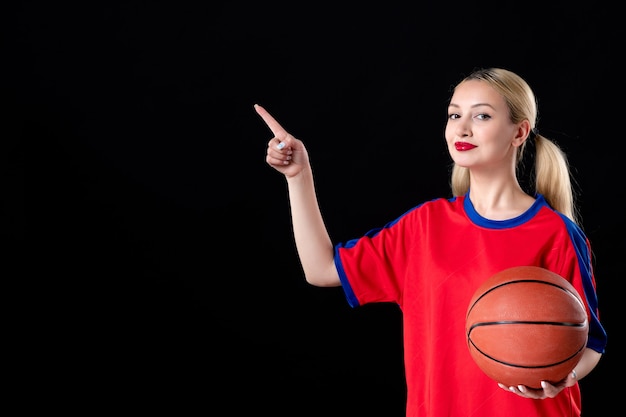 Basketballspielerin in Sportkleidung mit Ball auf schwarzem Hintergrund spielen