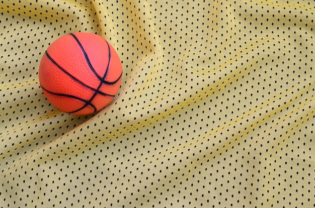 Basquete de borracha laranja pequeno encontra-se em uma camisa esporte amarelo