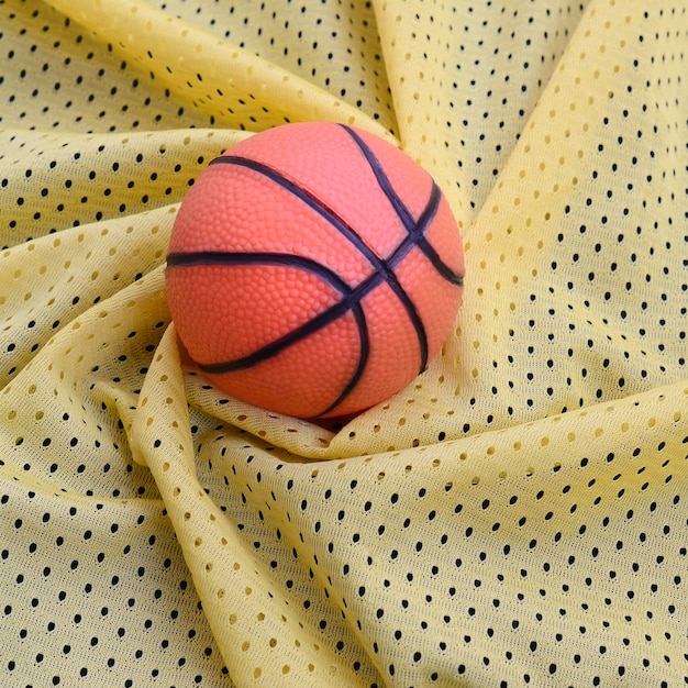 Basquete de borracha laranja pequeno encontra-se em uma textura de tecido de roupa esporte jersey amarelo e fundo com muitas dobras