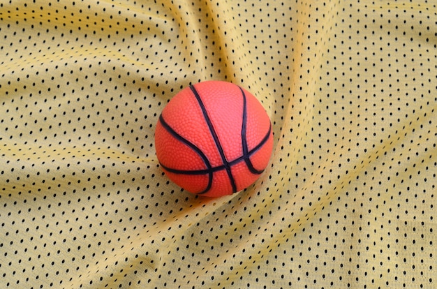 Basquete de borracha laranja pequeno encontra-se em uma textura de tecido de roupas esporte amarelo jersey