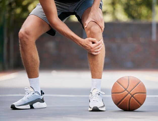 Basquetebol de dor e homem com lesão no joelho em pé na quadra ao ar livre, segurando a perna Aptidão esportiva e atleta com dor nas articulações ferido e machucado no treino e jogo na quadra de basquete