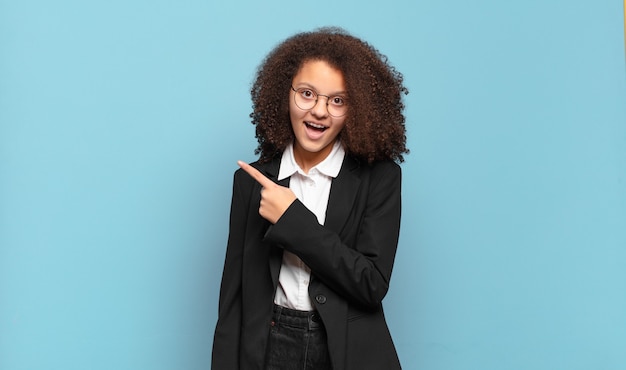 Bastante adolescente afro mirando emocionado y sorprendido apuntando hacia un lado y hacia arriba para copiar el espacio. concepto de negocio humorístico