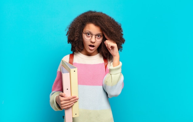 Bastante adolescente afro mirando sorprendido, con la boca abierta, conmocionado, dándose cuenta de un nuevo pensamiento