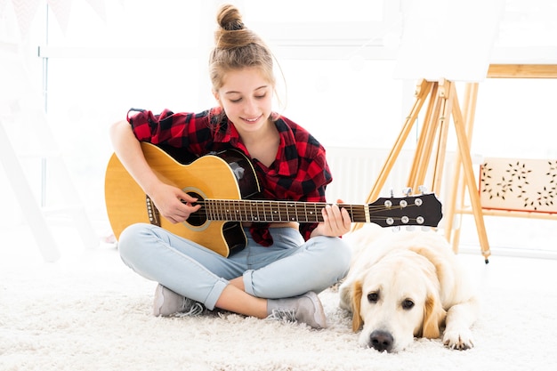 Bastante adolescente tocando la guitarra junto al lindo perro en casa