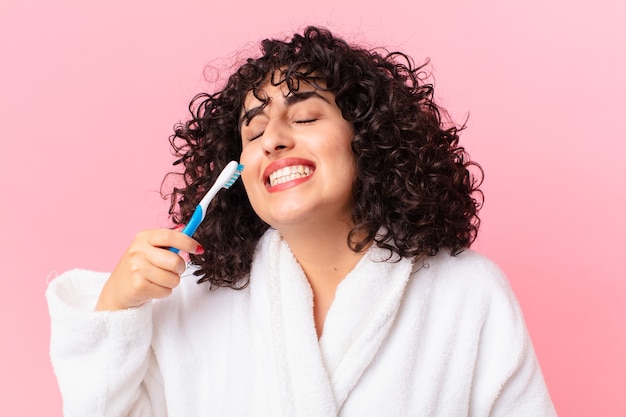 Bastante árabe mujer vistiendo albornoz y usando un cepillo de dientes