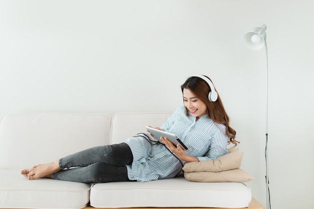 Bastante asiática escuchando música en el sofá en casa en la sala de estar