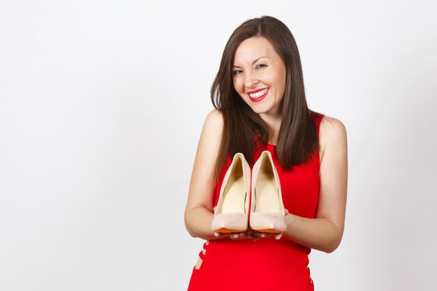 Bastante glamour caucásico moda joven mujer de cabello castaño en vestido rojo con zapatos beige con suela roja de sus compras en las palmas de las manos aisladas sobre fondo blanco. Copie el espacio para publicidad.