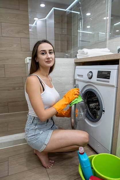 Bastante joven ama de casa con guantes protectores amarillos limpia la lavadora