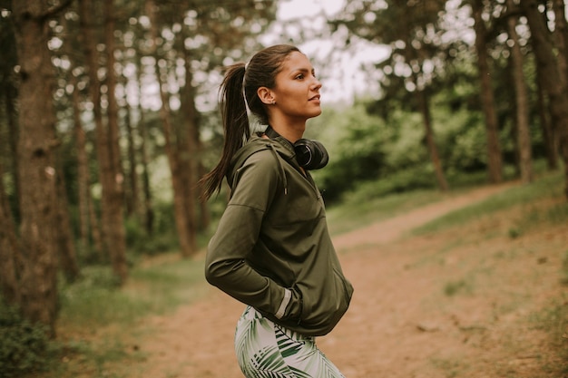 Bastante joven y atractiva corredora escuchando música y tomando un descanso después de trotar en un bosque
