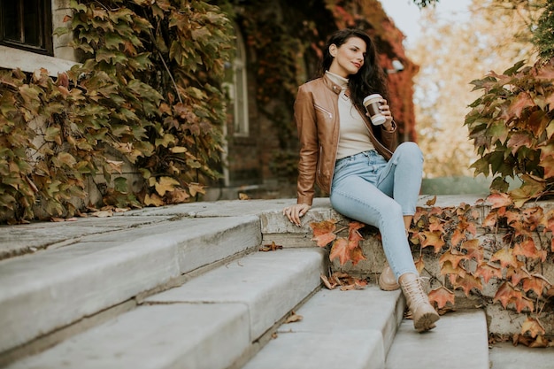 Bastante joven bebiendo café para llevar en las escaleras exteriores el día de otoño