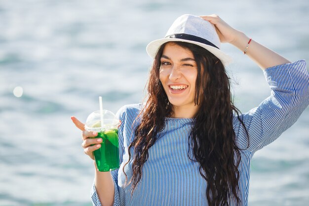 Bastante joven bebiendo cócteles en la playa. Chica atractiva que ofrece una bebida. Hermosa mujer bebiendo limonada