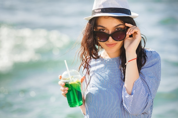 Bastante joven bebiendo cócteles en la playa. Chica atractiva que ofrece una bebida. Hermosa mujer bebiendo limonada