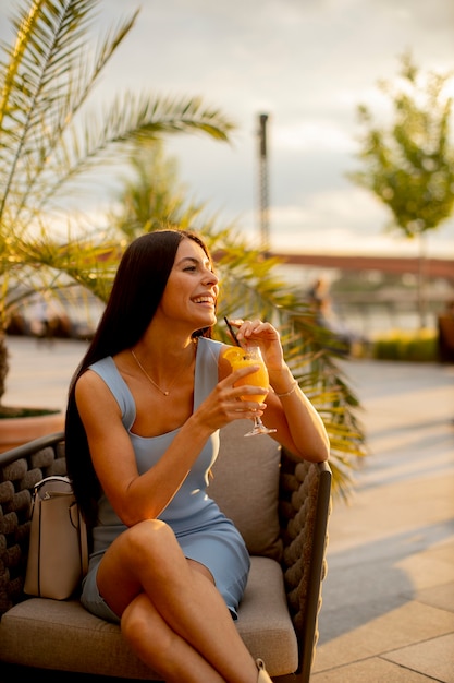 Foto bastante joven bebiendo jugo de naranja en el café de la calle