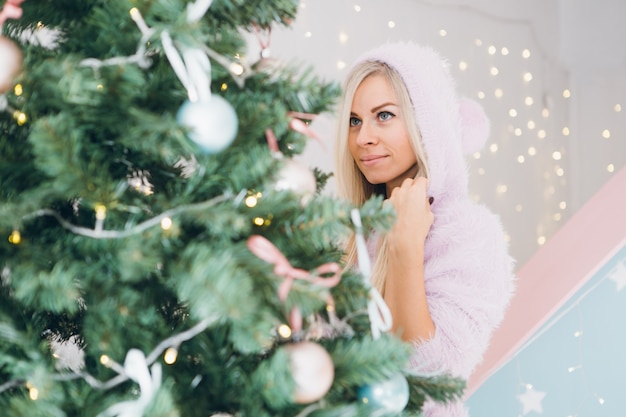 Bastante joven con cabello rubio está decorando un árbol de Navidad