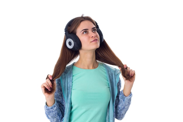 Bastante joven en camisa azul escuchando la música en auriculares negros y mirando hacia arriba en el estudio