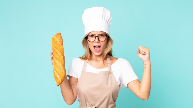 Bastante joven chef rubia mujer sosteniendo una baguette de pan