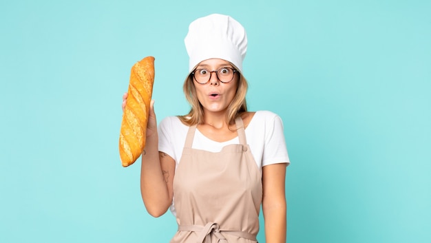 Bastante joven chef rubia mujer sosteniendo una baguette de pan