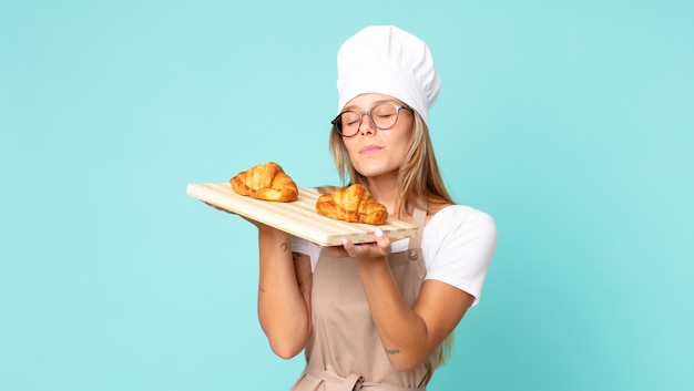 Bastante joven chef rubia sosteniendo una bandeja de croissants