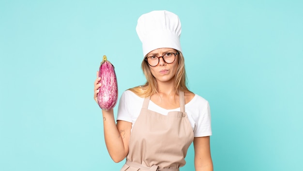 Bastante joven chef rubia sosteniendo una berenjena