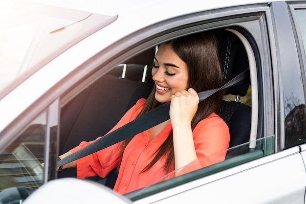 Bastante joven conduciendo su auto nuevo. Cinturón de seguridad de sujeción femenina en coche