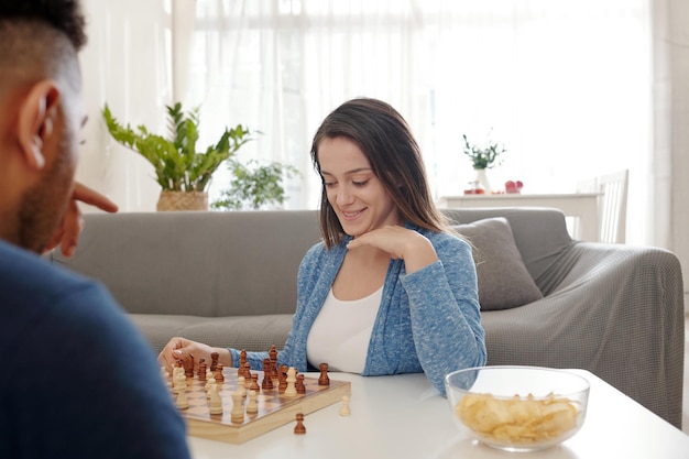 Bastante joven disfrutando jugando al ajedrez y comiendo papas fritas con su novio en casa