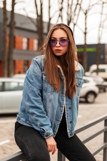 joven elegante hermosa mujer inconformista en glamorosos vidrios púrpuras en ropa de jeans de moda