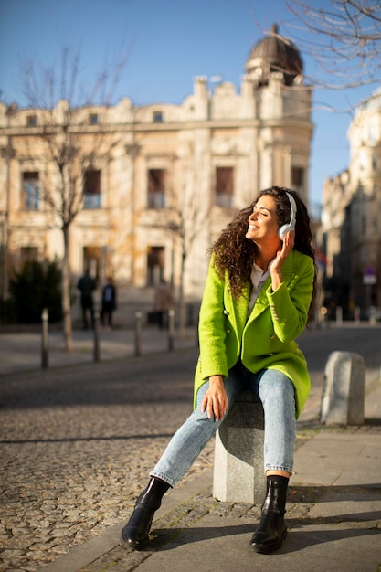 Bastante joven escuchando música con teléfono inteligente en la calle y sosteniendo café para llevar