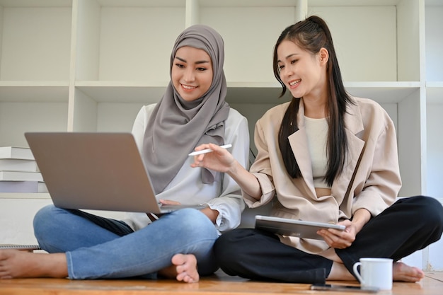 Bastante joven estudiante universitaria asiática en el espacio de coworking de la biblioteca con su amiga musulmana