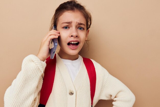 Bastante joven hablando por teléfono con una mochila de fondo beige