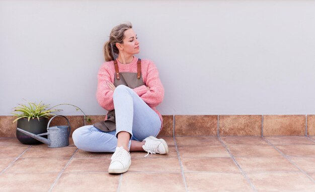 Foto bastante joven jardinería y sentada en el suelo al aire libre