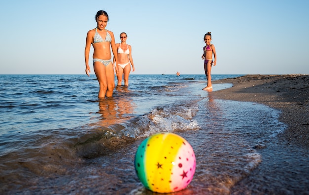 Bastante joven juega a la pelota con sus encantadoras hijas mientras nada en el mar en un cálido día de verano soleado