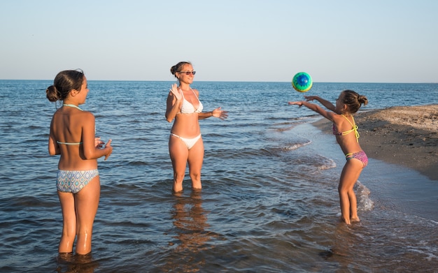 Bastante joven juega a la pelota con sus encantadoras hijas mientras nada en el mar en un soleado día de verano. Concepto de vacaciones con niños.