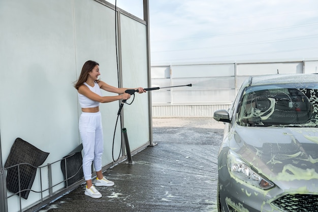 Bastante joven lavando su coche en la estación de lavado de coches