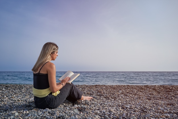 Bastante joven leyendo un libro en la playa