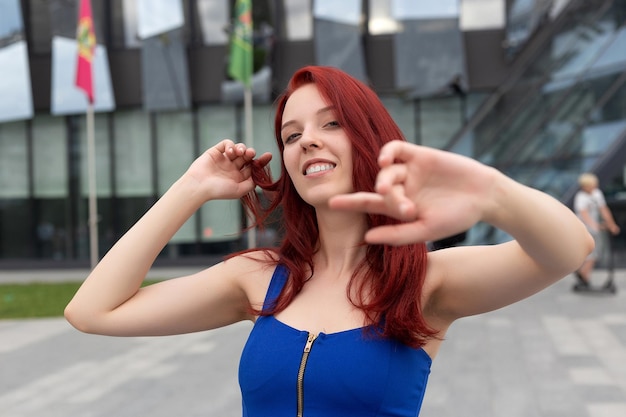 Bastante joven con un maravilloso sentido del humor cabello rojo y un vestido azul en una calle de la ciudad riéndose de la cámara